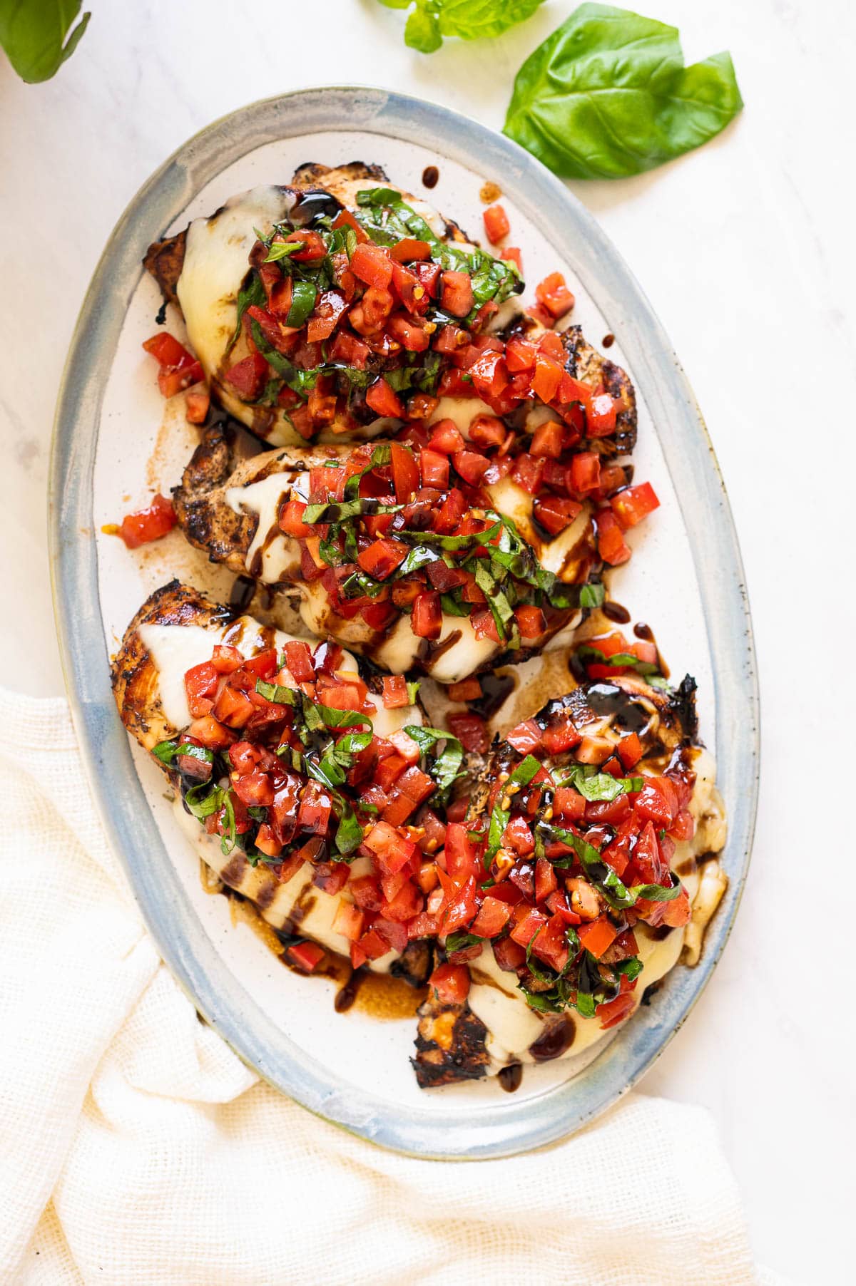 Grilled chicken breasts topped with melted cheese and bruschetta served on a platter.