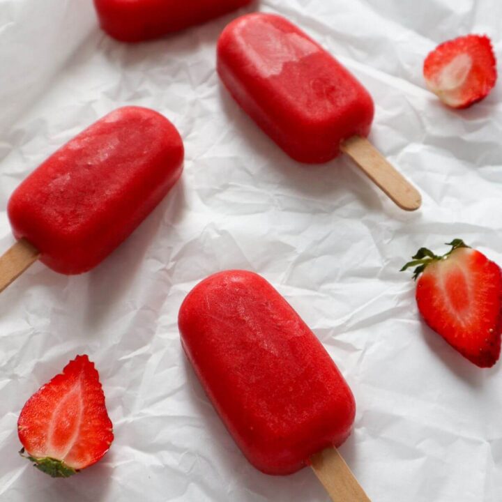 Strawberry ice cream popsicles with wooden sticks on white paper.