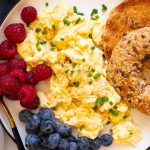 Cottage cheese scrambled eggs served on a plate with raspberries, blueberries and toasted bagel.