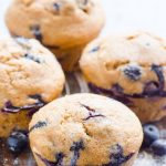 Four healthy blueberry muffins on a counter with fresh blueberries.